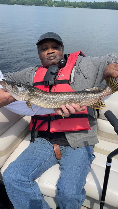 Day services client proudly holding a caught northern pike during a fishing activity